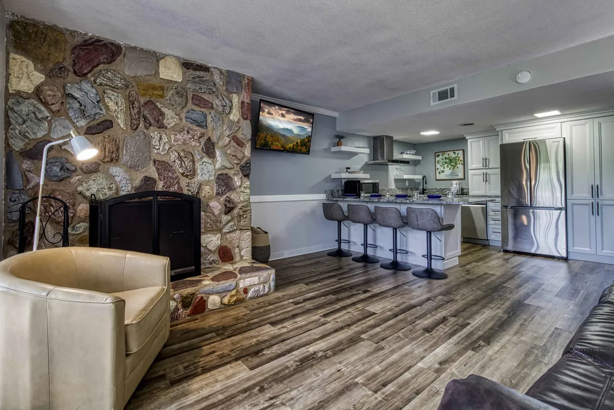 This interior scene highlights a stone fireplace adjacent to a set of bar stools and modern kitchen appliances, all within a cozy and stylish kitchen-dining space. The space feels perfect for intimate meals or socializing over dinner.