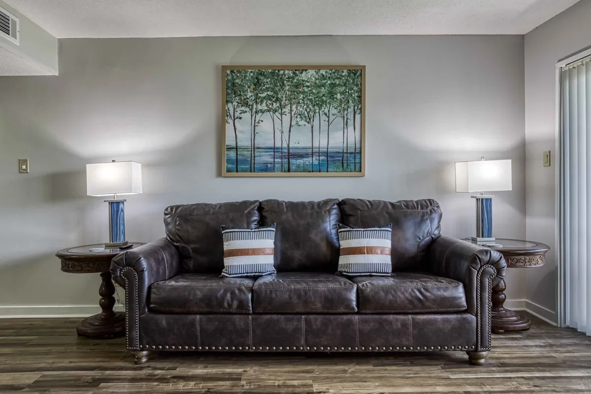 The image showcases a warm, inviting living space with a plush leather sofa, tasteful mountain-inspired artwork, and soft table lamps casting a cozy glow—perfect for unwinding after a day in the Smokies.