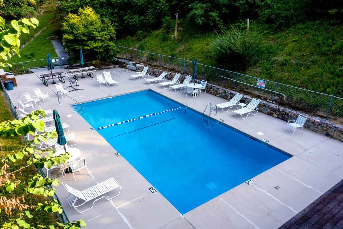 A sparkling swimming pool is surrounded by lounge chairs and tables with umbrellas, creating a welcoming setting for swims, sunbathing, and social gatherings in a relaxed atmosphere. The pool area is open and inviting, ideal for unwinding or connecting with neighbors.