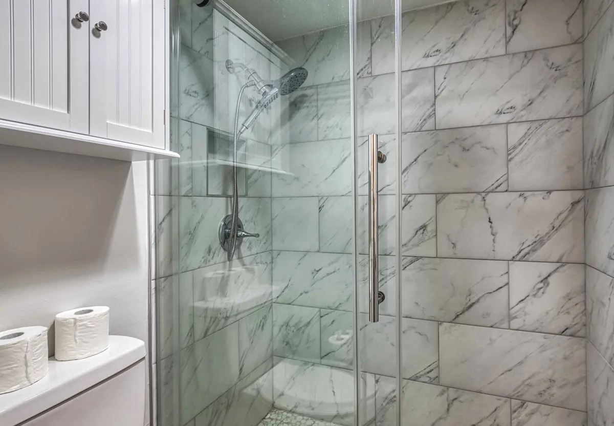 A modern bathroom featuring a glass shower enclosure, marble tiles, white cabinets, and a neat layout. The clean lines and soft lighting evoke a sense of luxury and calm, perfect for unwinding at the end of the day.